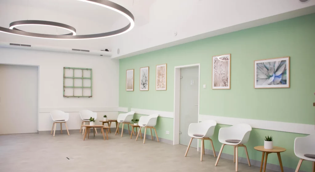 Zahnzusatzversicherung – moderner Wartebereich im Zahnzentrum Wien mit grüner Wand, Designerstühlen und heller Deckenbeleuchtung.